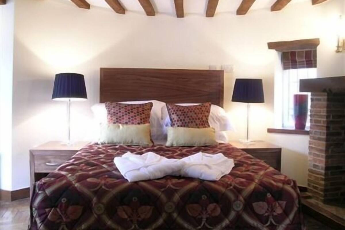 A bedroom with a wooden headboard, two bedside lamps, a patterned bedspread, and a fireplace.