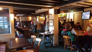 A cozy restaurant with wooden tables and chairs, a bar area, and a television screen. - Ye Olde Red Lion (Newbury)