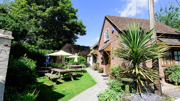 A brick house with a garden, picnic tables, and a large tree. - Ye Olde Red Lion (Newbury)