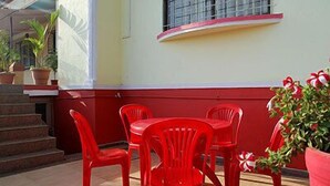 A patio with red plastic chairs and a table, a staircase, and a building with a red and white facade. - Shanti's Hotel Sonai (Mahabaleshwar)