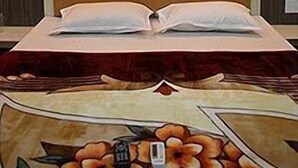 A bed with a headboard, two bedside lamps, and a floral-patterned bedspread. - Shanti's Hotel Sonai (Mahabaleshwar)