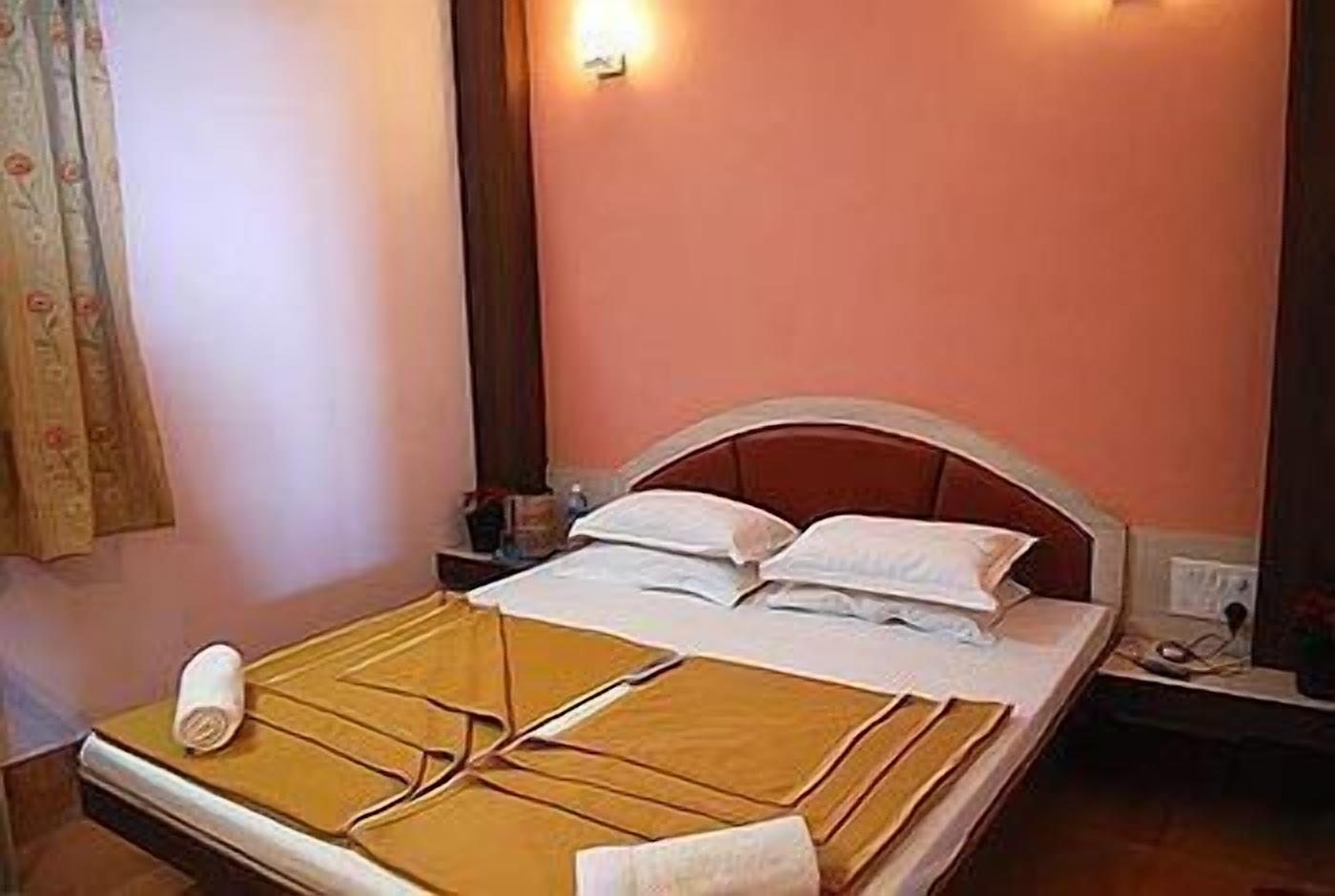 A neatly made bed with pillows and a rolled-up towel, a nightstand with a lamp, and a wall-mounted light fixture.