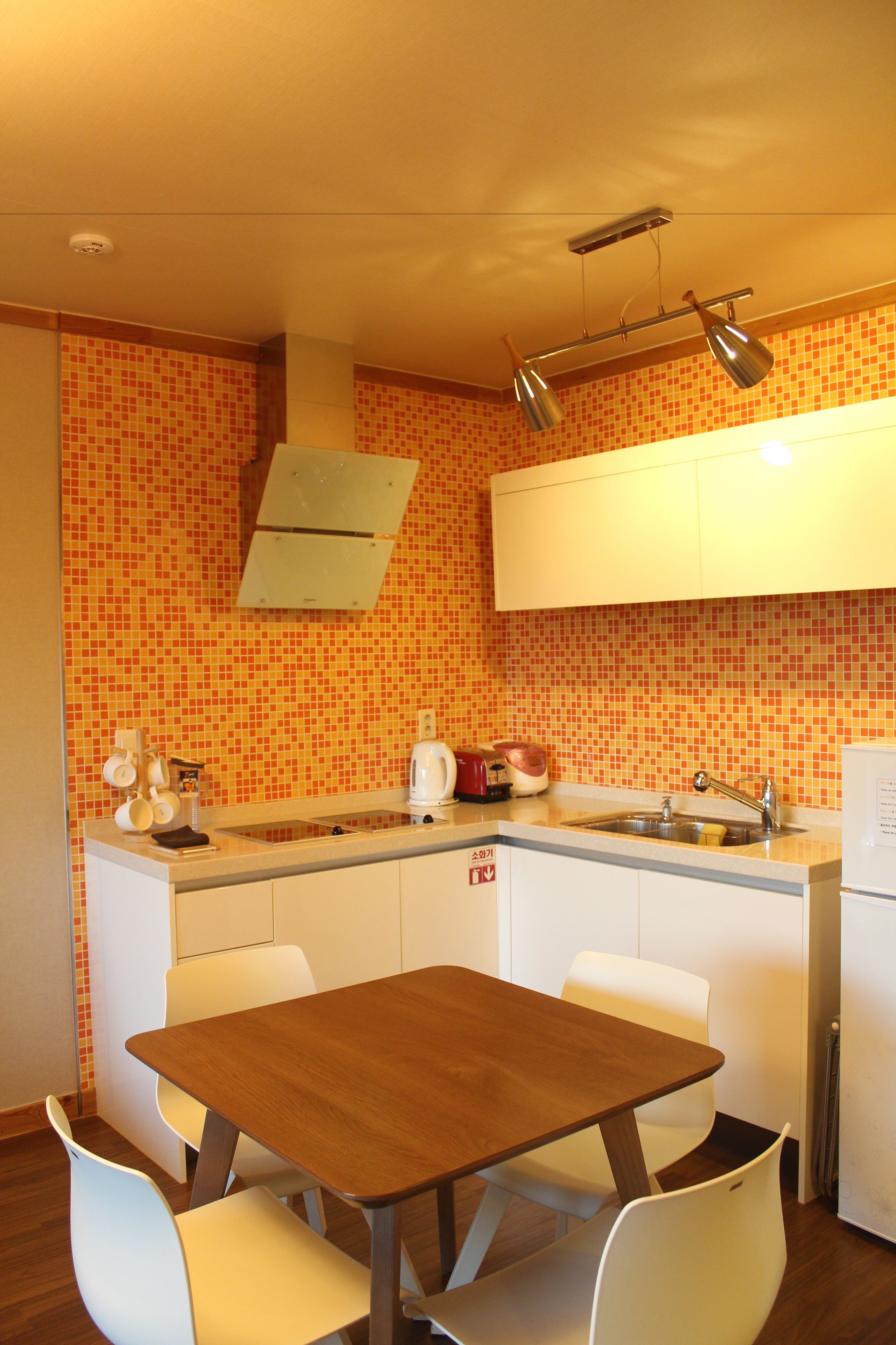 A kitchen with a tiled backsplash, a wooden table, white chairs, a sink, and a refrigerator.