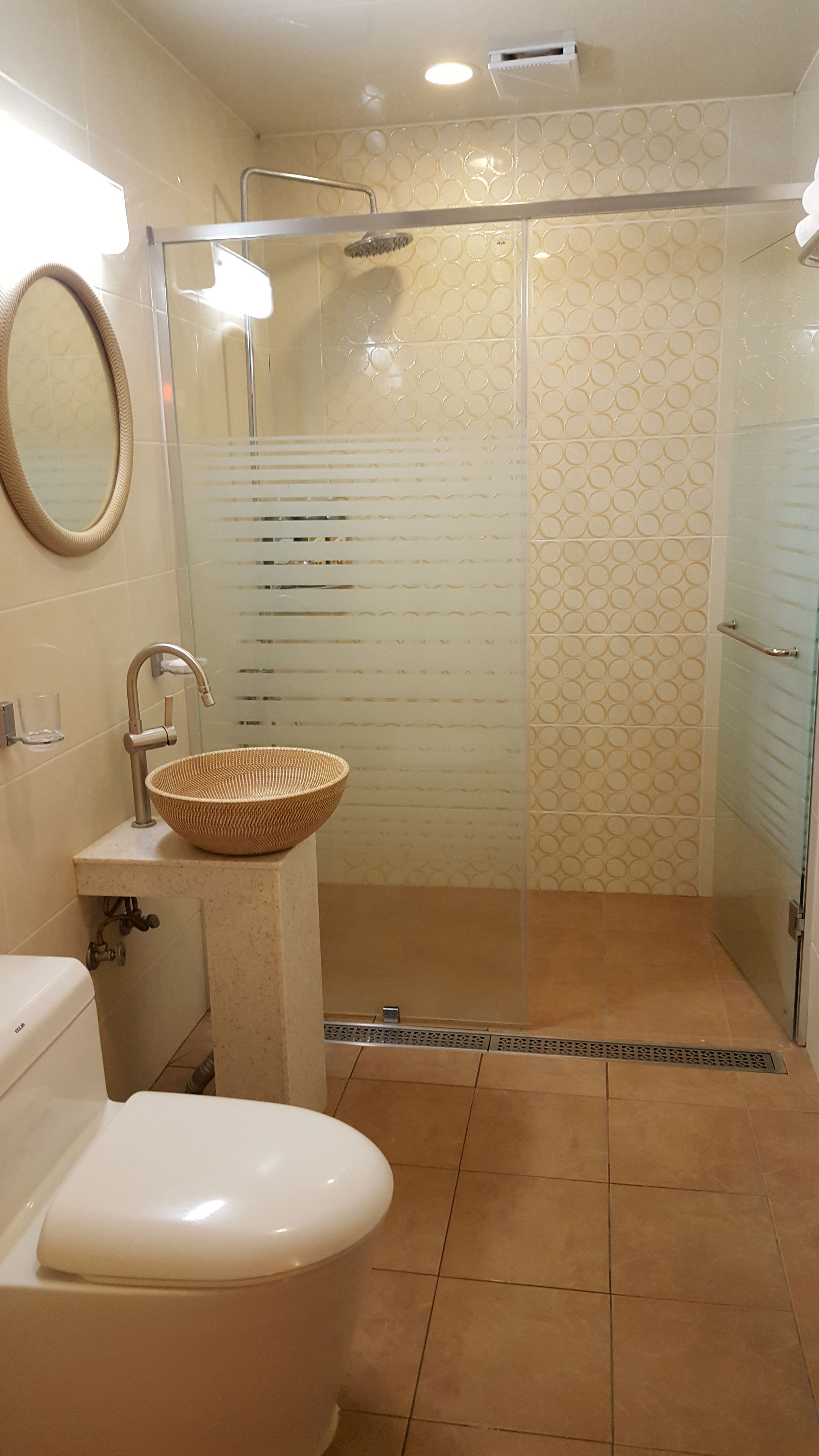 Ein Badezimmer mit Toilette, einem Waschbecken mit geflochtener Schüssel, einer Dusche mit Glastür und gemusterten Fliesen.