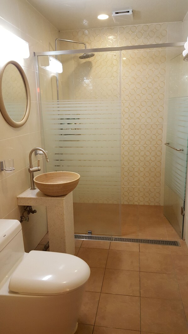 Un baño con inodoro, lavabo con recipiente tejido, ducha con puerta de cristal y azulejos estampados.