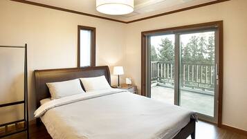 Habitación de hotel con una cama grande, una mesita de noche con lámpara, una ventana con vistas a un balcón y un ventilador de techo.
