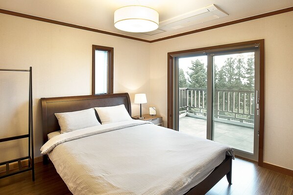 Habitación de hotel con una cama grande, una mesita de noche con lámpara, una ventana con vistas a un balcón y un ventilador de techo.