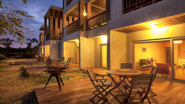 Un edificio moderno con terraza de madera, asientos al aire libre y un balcón.