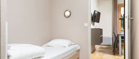 A small, clean room with a single bed, a flat-screen TV mounted on the wall, and a wooden floor.