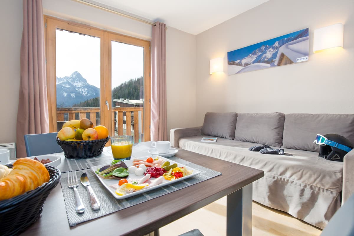 A breakfast setup with a table, breakfast items, and a view of mountains through a window.