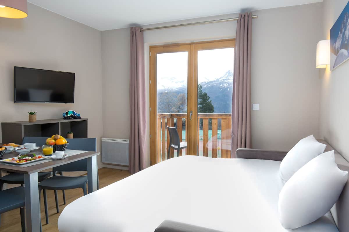 A hotel room with a bed, a desk with breakfast, a TV, and a balcony with a mountain view.