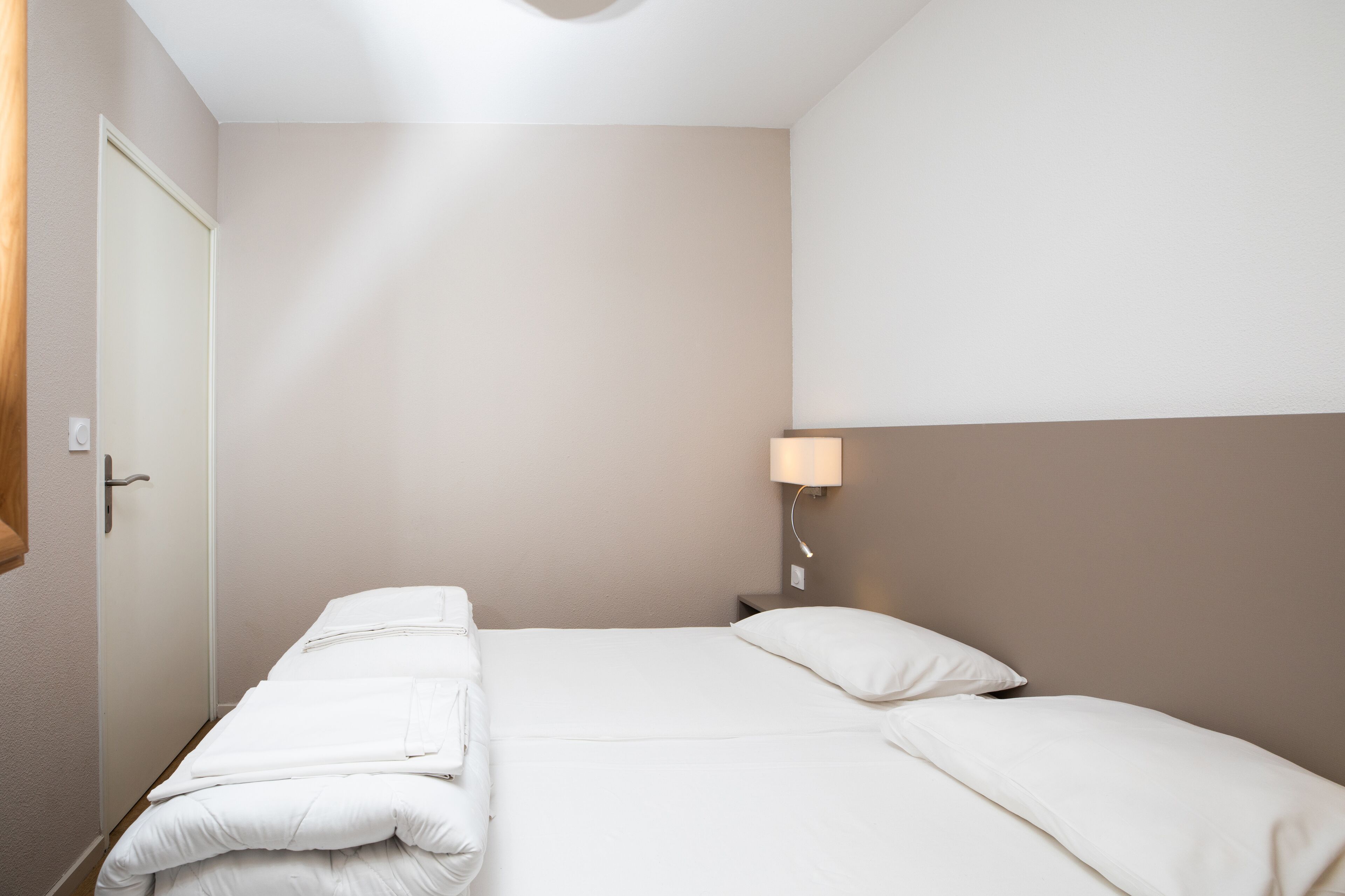 Una habitación de hotel con cama, mesita de noche, lámpara y puerta.