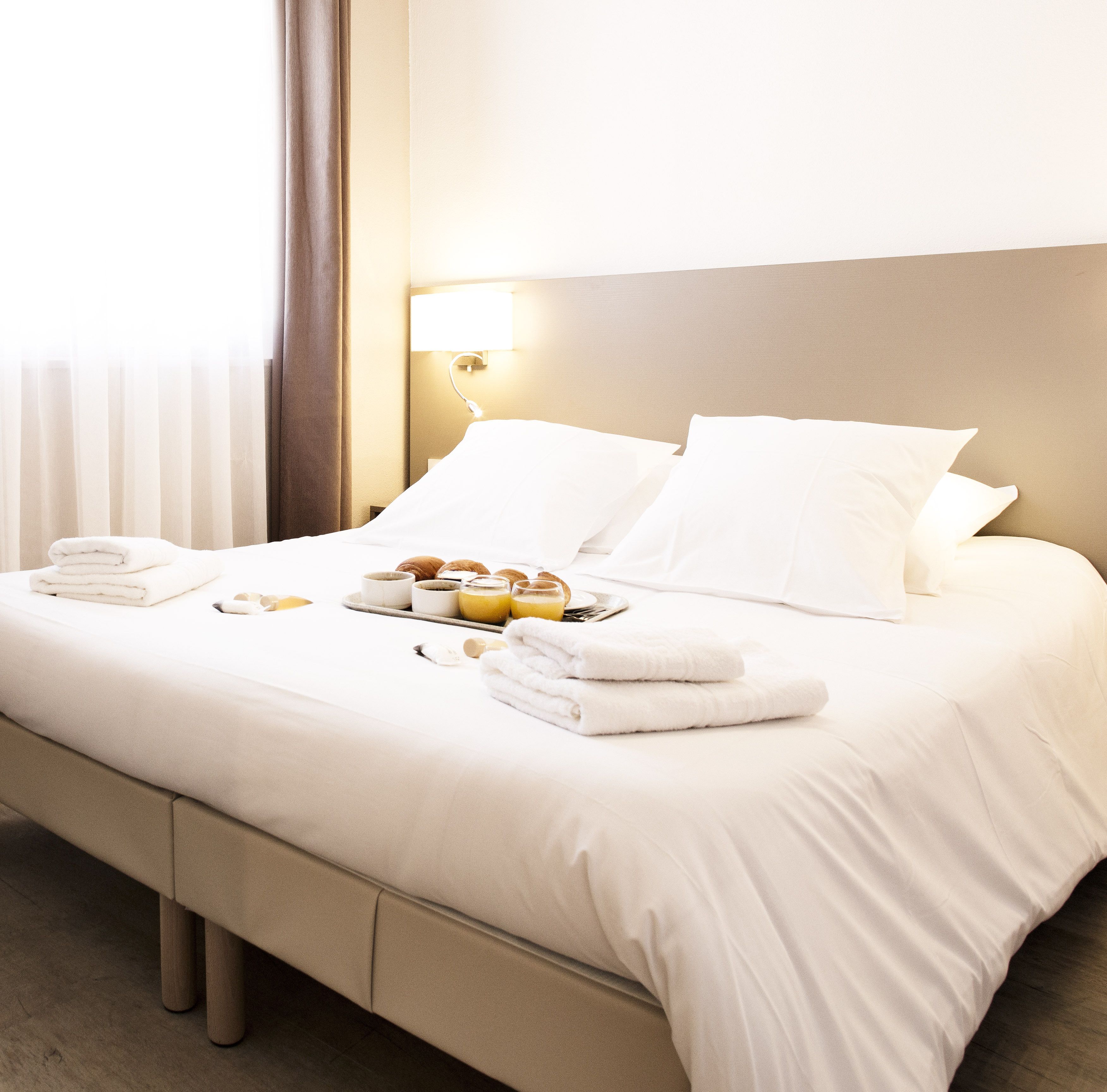 Een net opgemaakt bed met witte lakens, een tray met toiletartikelen en een bedlampje.