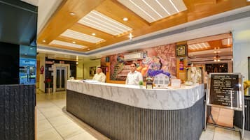 A hotel reception desk with a marble counter, wooden ceiling, and a mural of deities.