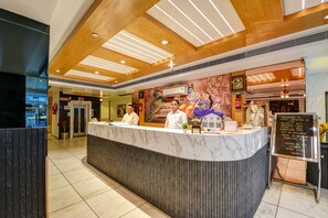A hotel reception desk with a marble counter, wooden ceiling, and a mural of deities. - Hotel Krishna Deluxe (New Delhi)