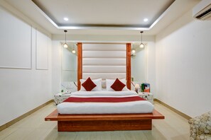 A modern bedroom with a wooden bed frame, white bedding, and a large mirror above the bed. - Hotel Krishna Deluxe (New Delhi)