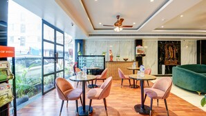 Un restaurante moderno con amplios ventanales, suelo de madera y un ventilador de techo. Mesas y sillas dispuestas para comer.