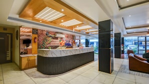 Zona de recepción de un hotel con un mostrador de mármol, techo de madera y un mural de un pavo real.