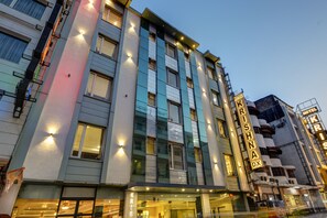 A multi-story hotel with illuminated signage, large windows, and a modern facade. - Hotel Krishna Deluxe (New Delhi)