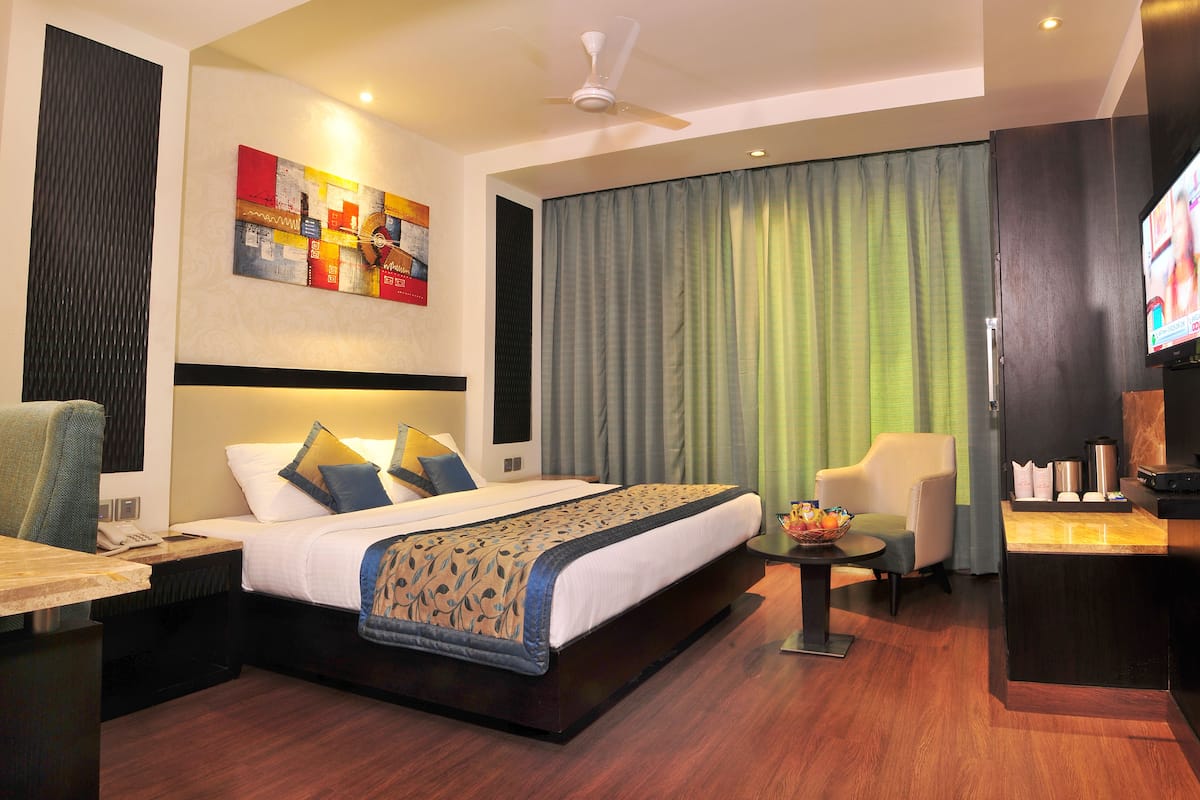 A hotel room with a bed, a desk, a chair, a television, and a window with curtains.