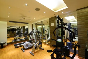 A modern gym with various exercise equipment, including treadmills and weight machines, and a large mirror wall.
