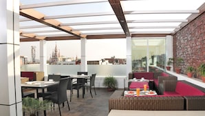 A rooftop patio with outdoor seating, a view of a cityscape, and a brick wall. - Hotel City Star (New Delhi)