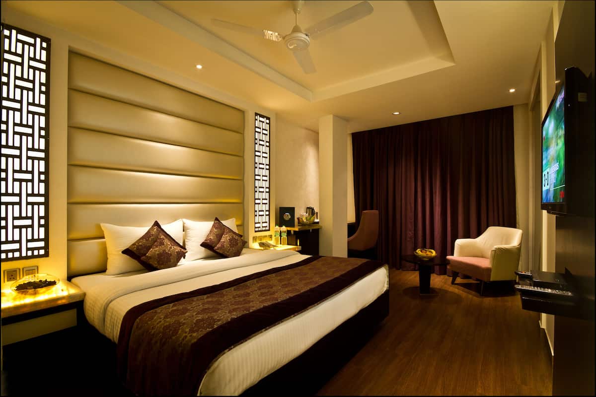 A hotel room with a large bed, a ceiling fan, a television, a desk with a lamp, and a chair.
