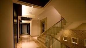 A modern interior with a glass staircase, a hallway leading to a door, and a patterned wall. - Hotel City Star (New Delhi)