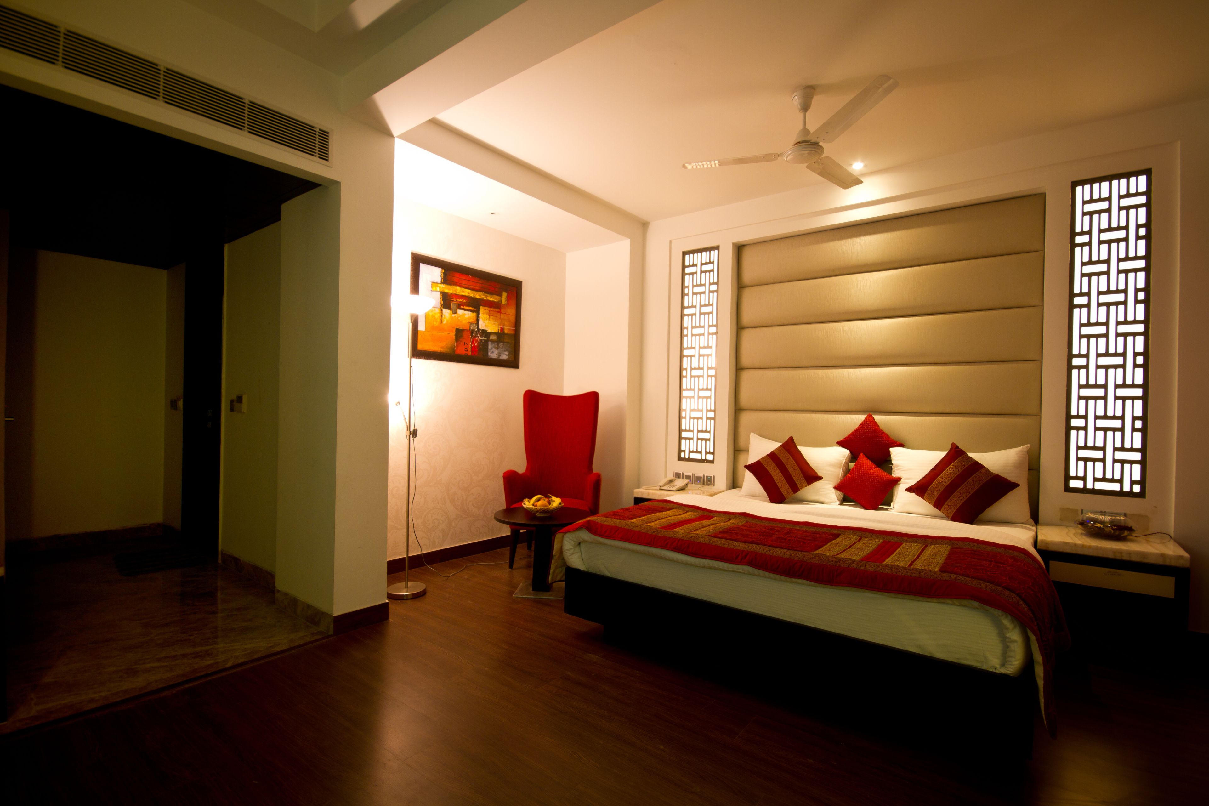 A hotel room with a large bed, a red armchair, a small table with fruit, and a painting on the wall.