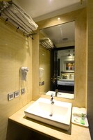 Een hotelbadkamer met een grote spiegel, een wastafel, een haardroger en een handdoekhouder.