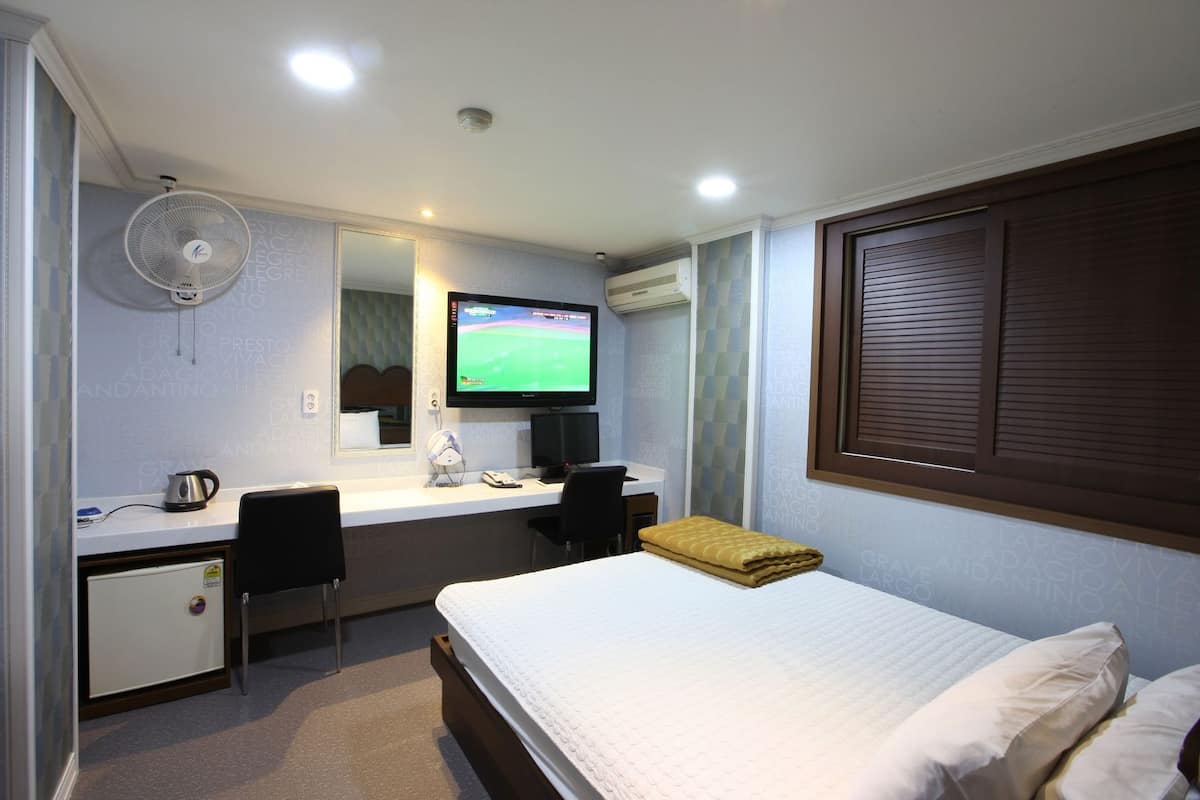 Habitación de hotel con cama, escritorio con computadora, televisión y aire acondicionado de pared.