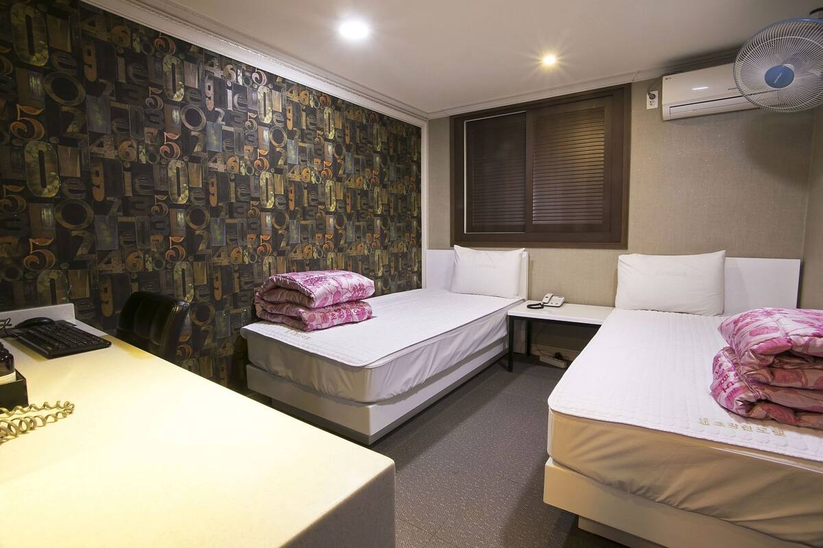 Habitación de hotel con dos camas, un escritorio con computadora, teléfono y aire acondicionado.