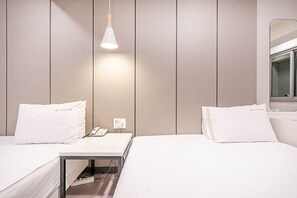 A hotel room with two beds, a bedside table with a phone, a hanging light fixture, and a mirror on the wall.