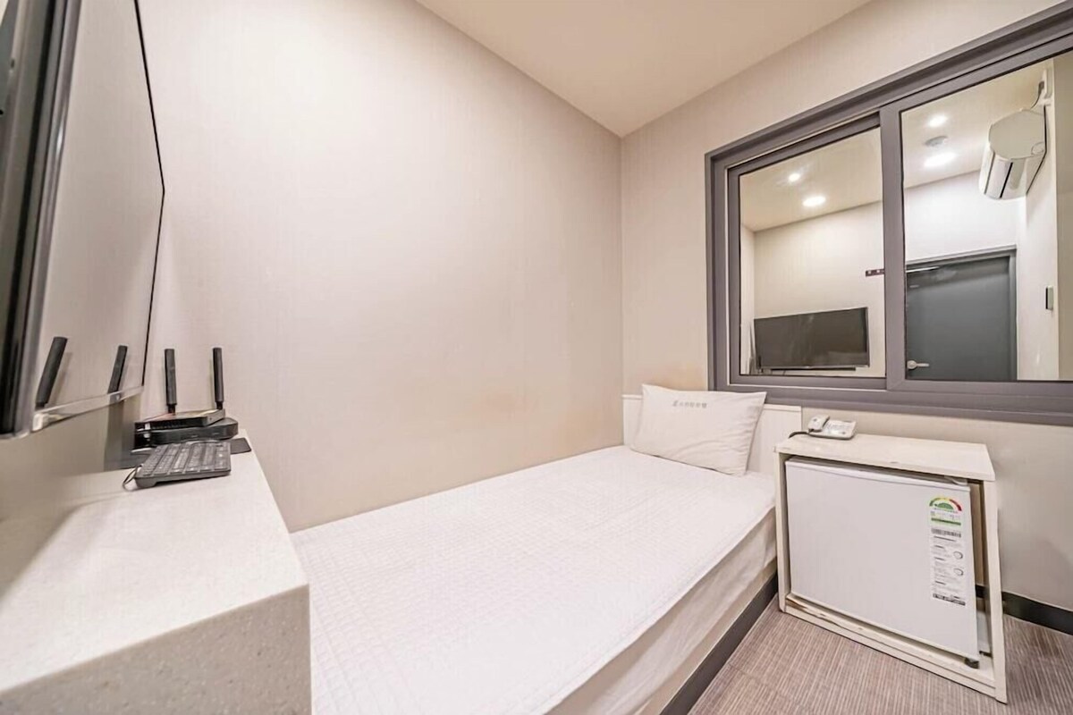 A small hotel room with a bed, a desk with a keyboard, a telephone, and a mini-fridge.