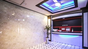 Un espace d’accueil avec un mur en marbre, une plante en pot, un comptoir portant l’inscription « RENSEIGNEMENTS » et un sol à motifs.