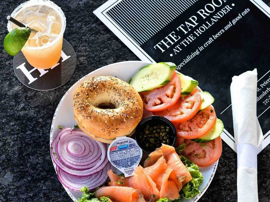 Ein Teller mit einem Bagel, Räucherlachs, Gemüse und einem Getränk, zusammen mit einer Speisekarte und einem Servietttuch.