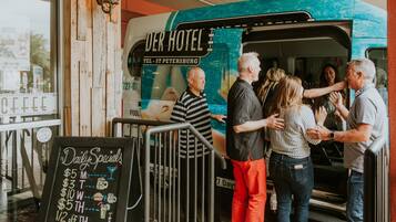 Un camion-restaurant, avec une enseigne indiquant « DER HOTEL » et « TÉL. – SAINT-PÉTERSBOURG », est stationné devant un immeuble.
