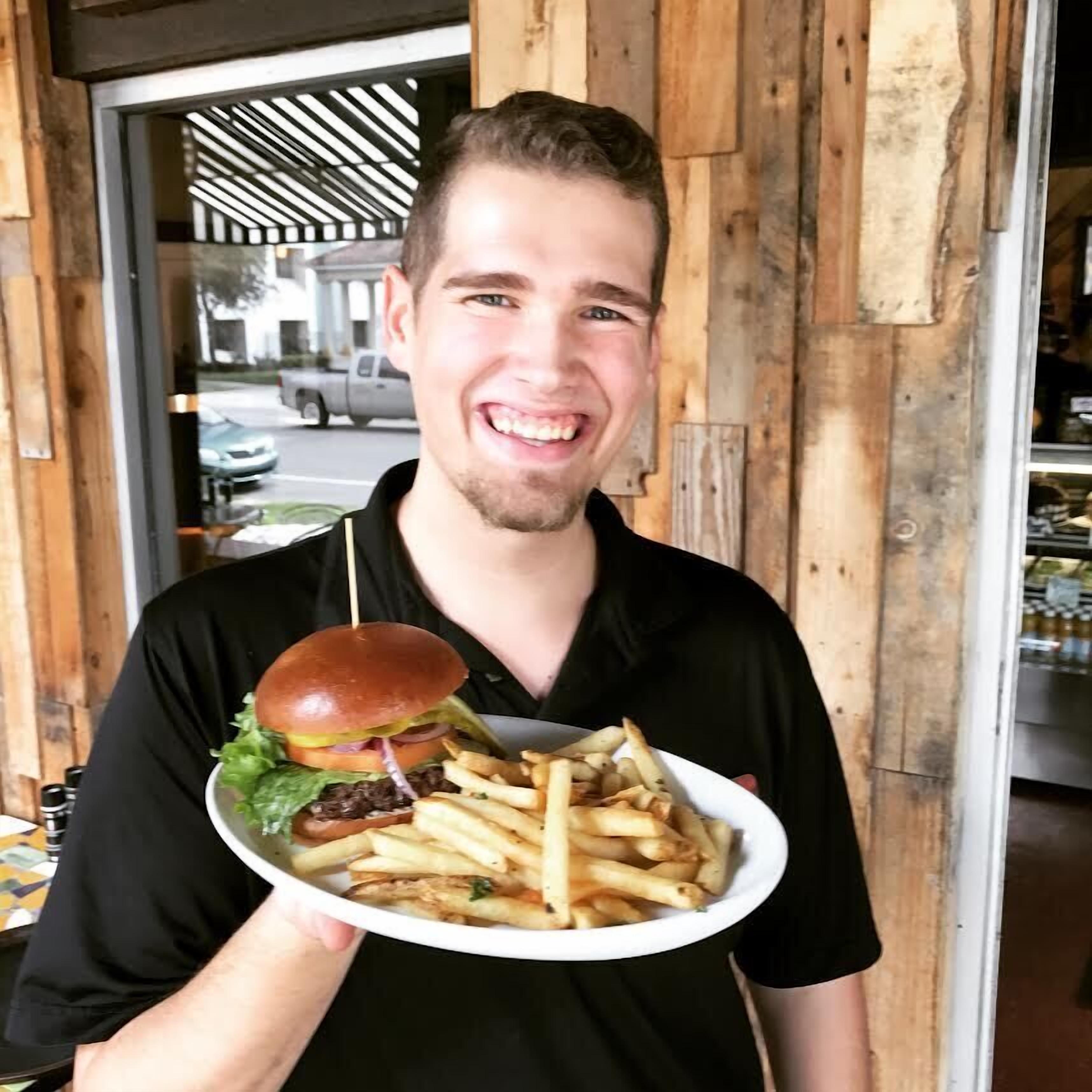 Una persona sosteniendo un plato con una hamburguesa y papas fritas.