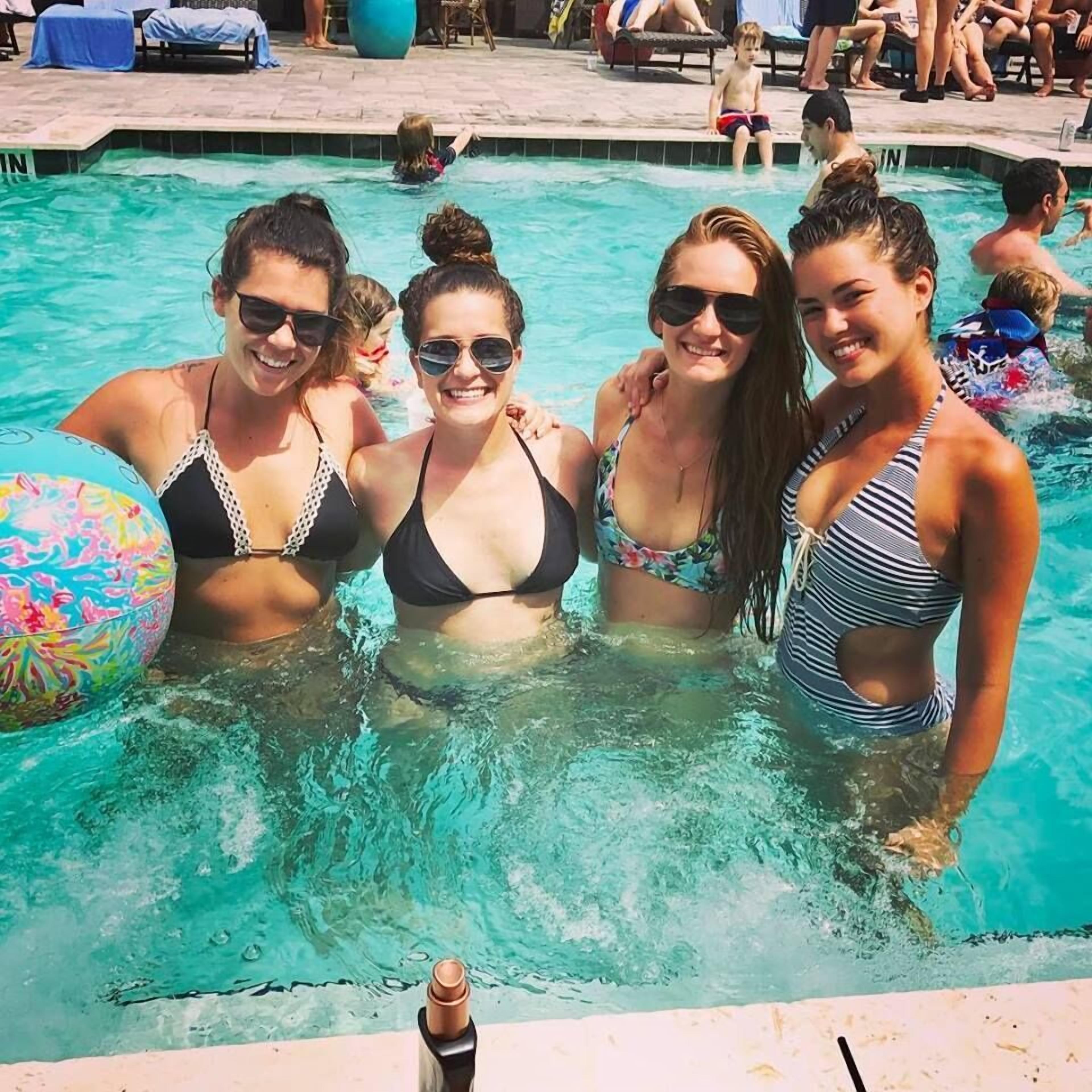 A swimming pool with people in the water and lounge chairs around the pool.