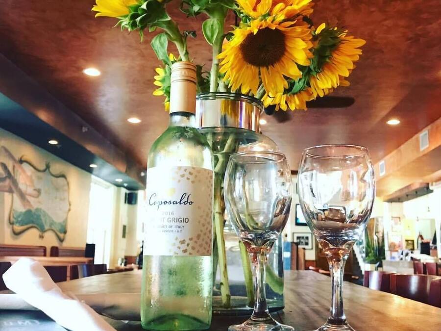 A table with a bottle of wine, two wine glasses, and a vase with sunflowers.