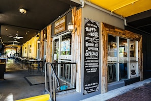 A café with outdoor seating, a chalkboard menu, and a sign indicating happy hour specials.