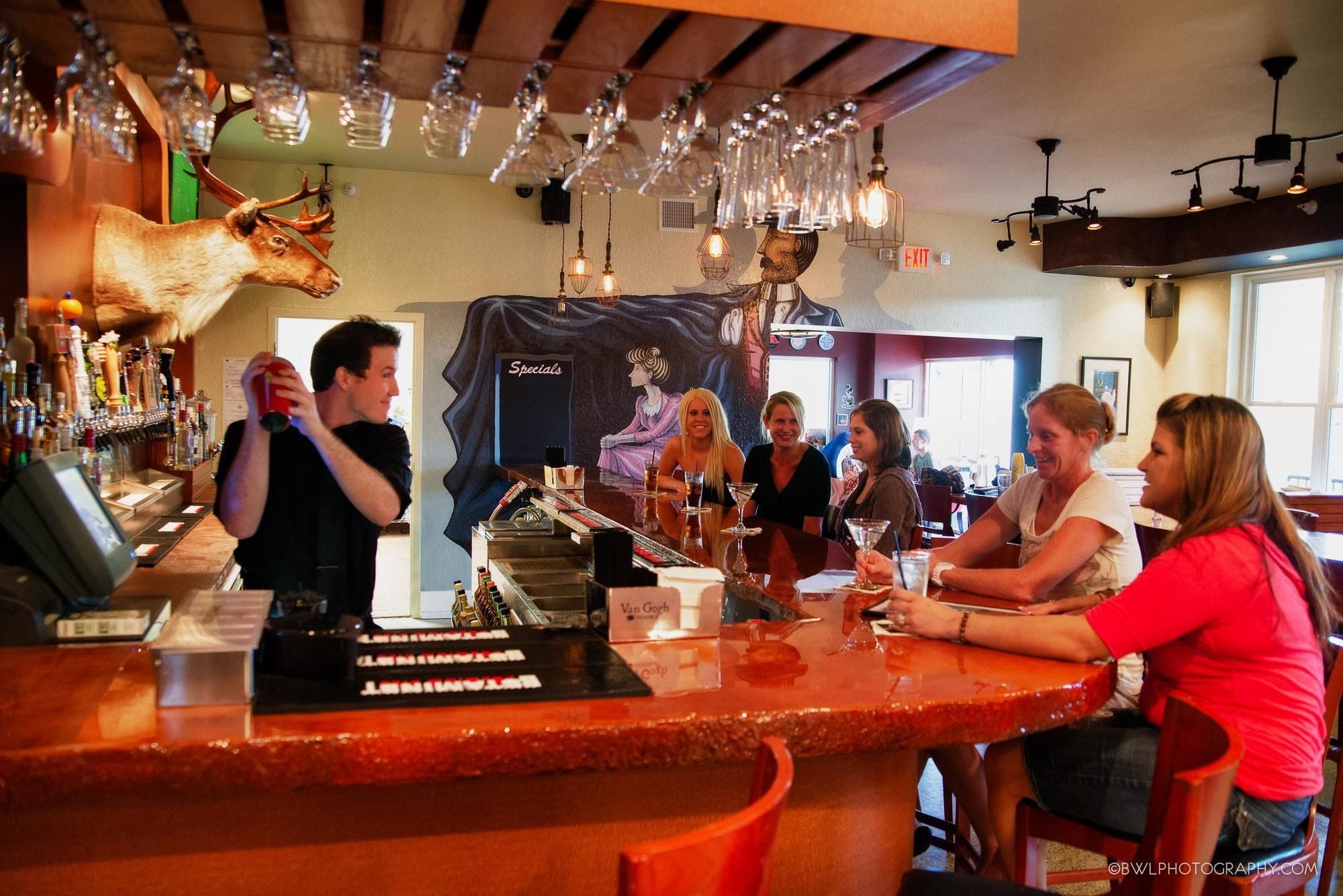 Un espace bar avec un comptoir, des luminaires suspendus et une tête de cerf fixée au mur.