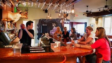 Un espace bar avec un comptoir, des luminaires suspendus et une tête de cerf fixée au mur.