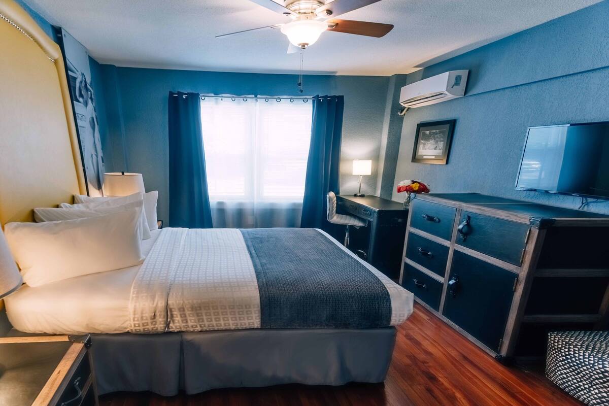 A hotel room with a bed, a desk, a television, and a ceiling fan.