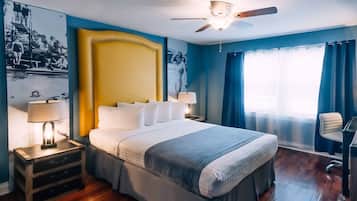 A hotel room with a large bed, a ceiling fan, a desk, and a window with curtains.