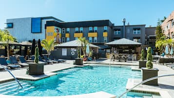 A hotel pool area with lounge chairs, a bar, and a building with a modern design.