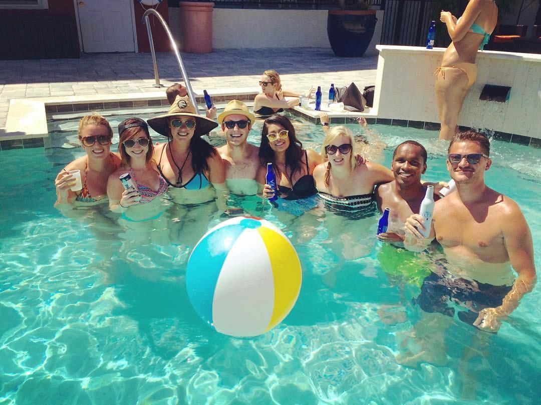 A group of people in a swimming pool with a beach ball, lounge chairs, and a poolside area.