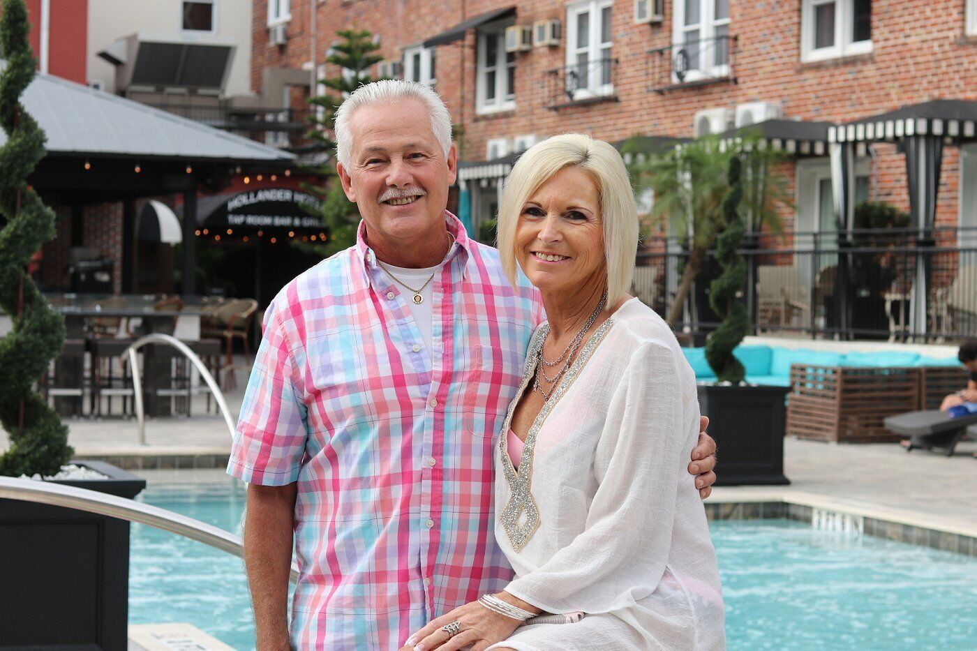 Un hombre y una mujer están junto a una piscina, con un restaurante al fondo.