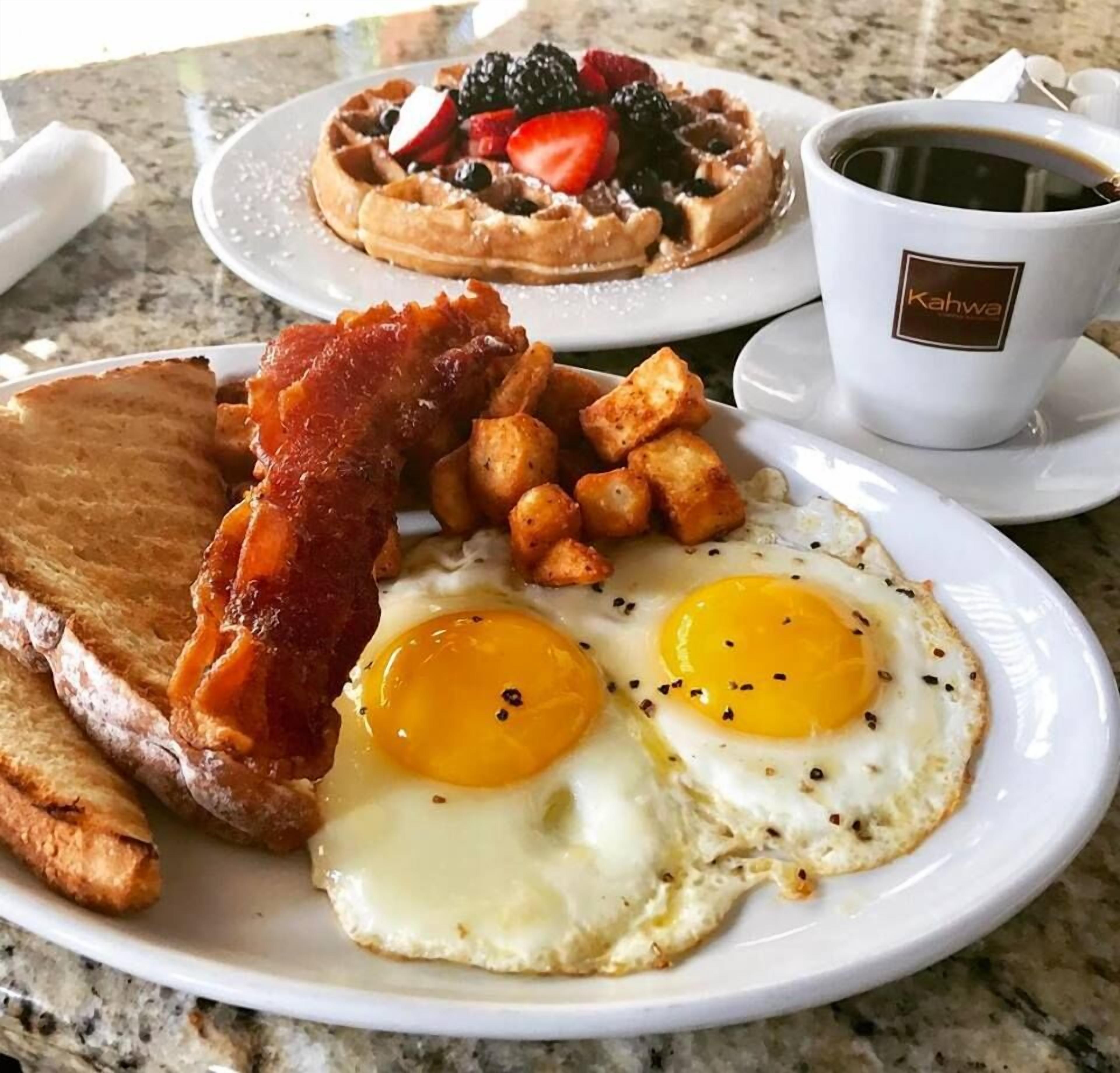 Un plato de desayuno con huevos, tocino, tostadas, patatas ralladas y un gofre con frutos rojos.
