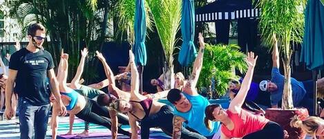 Un groupe de personnes pratiquant un exercice de yoga en plein air, sur un sol carrelé, avec des palmiers en arrière-plan.